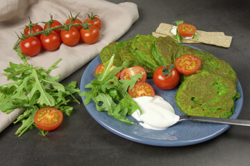 spinach and zucchini pancakes lie on a beautiful blue plate, decorated with a cherry tomato sprig, which lie on a cotton napkin. on a dark background