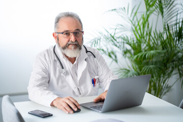 Senior Doctor looking a camera working with laptop and having a video conference with a patient. Telematic or online work concept.