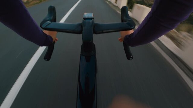 POV action shot of professional cyclist descend down steep dangerous mountain road.Cyclist in long sleeve jersey on carbon aero bike with integrated handlebar and computer ride very fast on empty road