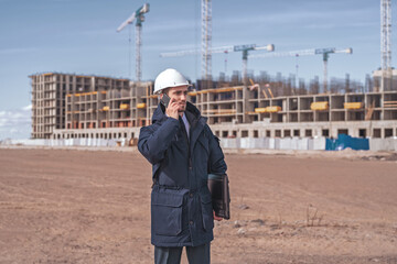 a civil engineer in a white helmet is talking on the phone in the background of construction.