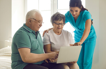 Caregiver, home care nurse or retirement home worker teaching happy senior patients to use modern computer. Old married couple looking at laptop screen and learning to browse medical Internet platform