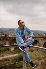 Stylish young man on the railway bridge in Vorokhta, Carpathians against the backdrop of a mountain landscape. tourists sitting in the mountains near the railway