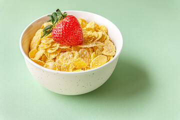 cornflakes and ripe juicy strawberry in a bowl on a light green surface