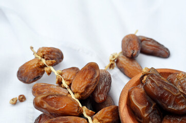 Dates (Phoenix dactylifera) on a wooden bowl on a white cloth background. food for breaking the fast during Ramadan for Muslims. selective focus