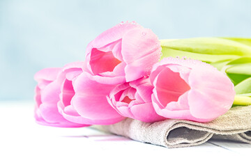 Festive bouquet of pink tulips lies on cloth on white table. Petals are covered with dew drops. Fresh flowers for gift