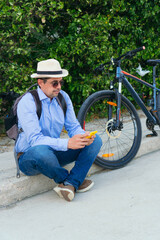 Obraz premium 40-year-old man checking his cell phone while sitting on the street with his bicycle