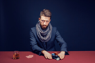 Stylish bearded Man in suit and scarf playing in dark casino, smoking cigar, drink whiskey