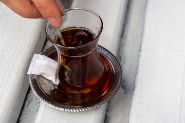 Black Turkish tea with piece sugar in traditional glass in Istanbul, Turkey. A man stirring hot tea with a small spoon. Top view, selective focus
