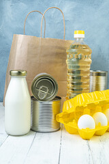 Grocery set for embroidery of an elderly person. Eggs in a yellow container, milk and canned food, bottle of oil on white board table. Food aid to the poor - 428437422
