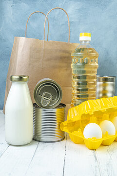 Grocery set for embroidery of an elderly person. Eggs in a yellow container, milk and canned food, bottle of oil on white board table. Food aid to the poor