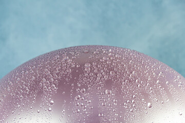 Hemisphere of pink balloon is covered with water drops against blue sky. Rainy holiday, event in cloudy weather