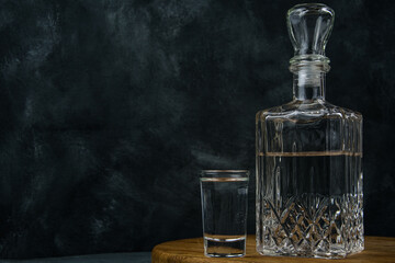 Glass of vodka on wooden table. Transparent decanter of beverage. Atmosphere bar drinking. Copy space for text on dark wall. Concept solitary alcoholism - obrazy, fototapety, plakaty