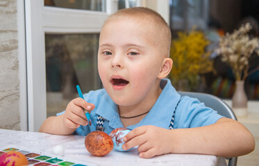 A boy with Down syndrome draws, a genetically ill child paints Easter eggs, preparation for Easter,...