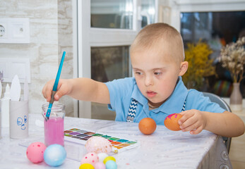 A boy with Down syndrome draws, a genetically ill child paints Easter eggs, preparation for Easter,...