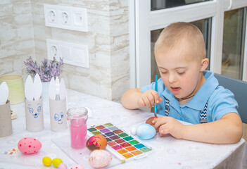 A boy with Down syndrome draws, a genetically ill child paints Easter eggs, preparation for Easter,...