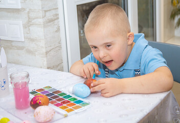 A boy with Down syndrome draws, a genetically ill child paints Easter eggs, preparation for Easter,...