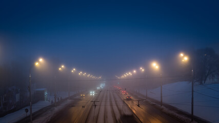 Fototapeta na wymiar Foggy misty road illuminated by street lights