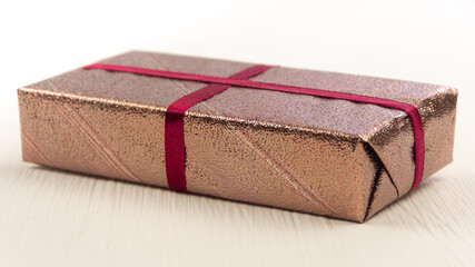 Gift box on white table. Romantic present in decorative pink foil, tied with satin ribbon