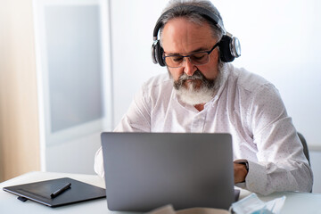 Senior man with headphone having a video conference with laptop at home