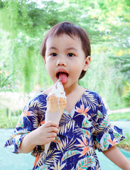 3 years old cute baby Asian girl sticking out her tongue and licking ice cream outdoor.