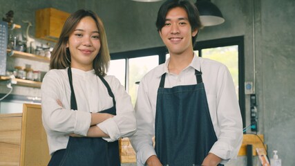 Fototapeta premium Portrait of young Asian colleague standing at their new business. Couple owner standing inside restaurant. Waitresses in aprons smiling standing together and looking at camera.