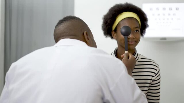 Smiling young woman african american doing eye test in ophthalmological clinics, holding occluder and looking at chart, Eyesight correction, Optics clinic, health concept.