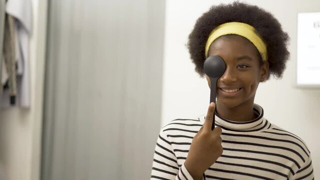 Smiling young woman african american doing eye test in ophthalmological clinics, holding occluder and looking at chart, Eyesight correction, Optics clinic, health concept.