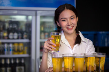 Beautiful Asian woman holding a glass of beer close up on background inside bar.