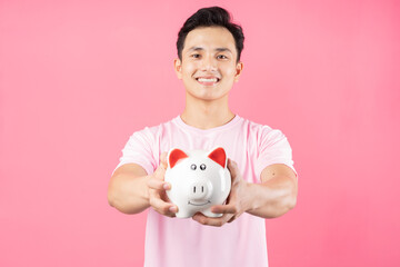Fototapeta na wymiar Young Asian man holding piggy bank on pink background