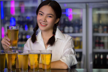 Beautiful Asian woman holding a glass of beer close up on background inside bar.