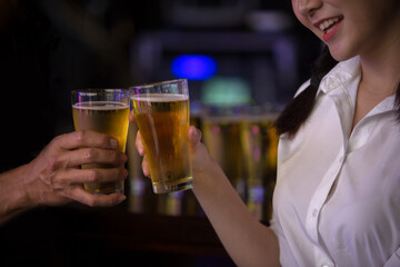 Beautiful Asian woman holding a glass of beer close up on background inside bar.