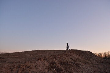 Silhouette of a playing boy with a roller playing with a scooter on a earthy hill at sunset