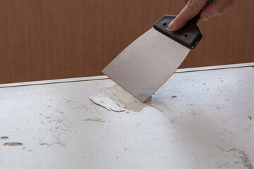 An anonymous person removes a layer of old paint with a spatula - obrazy, fototapety, plakaty