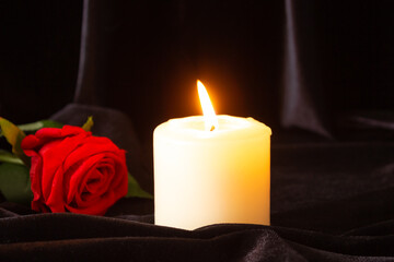 A burning candle and a red rose on a black background. The concept of condolences, mourning, and funerals.
