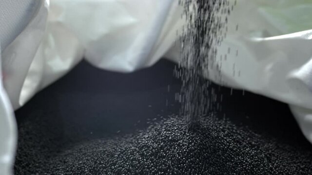 A man pours black polymer granules from his hands in a garbage recycling plant