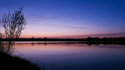 Beautiful landscape at sunset or sunrise. Symmetry of the sky and clouds in the water. Silhouette of tree in front of a lake.