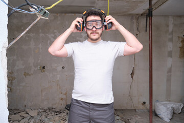 Young builder wearing hearing protection and safety glasses at a construction site. Safety at work.