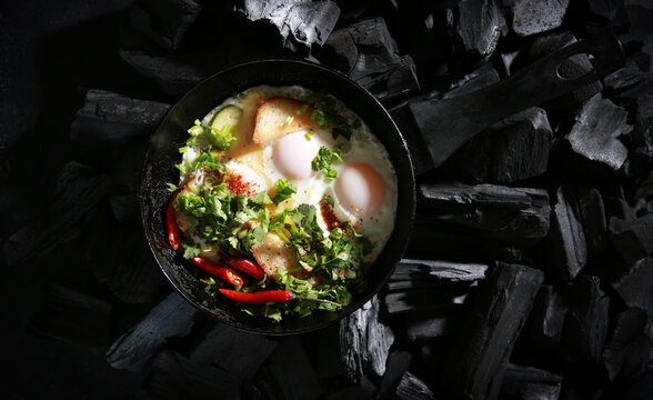 Russian cuisine. Breakfast: fried eggs with herbs, vegetables, bread, pepper in a black pan on black coals. Background image, copy space, flatlay, top view