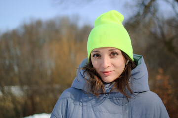 Lovely girl in a bright sports hat and winter coat posing against the backdrop of a winter forest or park
