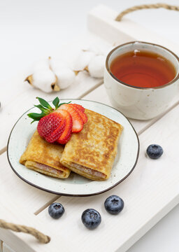 Russian rolled pancakes with strawberry filling. Served on a wooden tray with a cup of tea and berries. Top view. Vertical image.