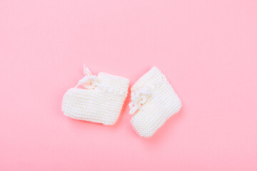 knitted baby booties on pastel pink background.