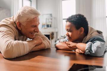 Man sitting at table with his multiracial son and looking at him with tenderness