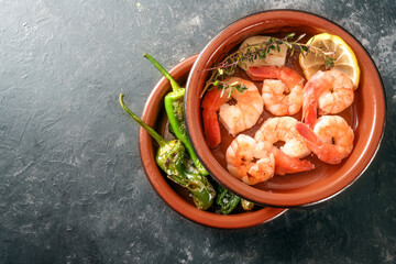 Shrimps and fried pimientos or padron peppers in stacked tapa bowls, traditional Spanish appetizer on a dark gray slate background, copy space, high angle view from above