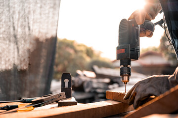 A carpenter using a drilling tool or an electric screwdriver is working at home on the wooden...