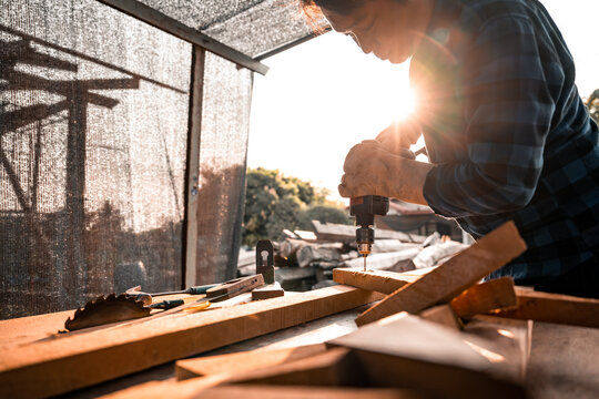 Close-up view A carpenter using a drilling tool or an electric screwdriver is working at home on the wooden floor. Ideas for home improvement and extension.