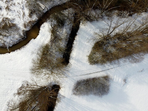 Aerial shot of a narrow river flowing through a snow-capped forest in winter - Powered by Adobe