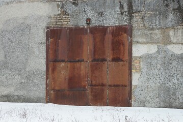 brown iron rusty closed gate on gray concrete garage wall in white snow on winter street