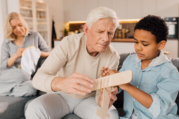 Man helping to his multiracial son making a wooden model of airplane
