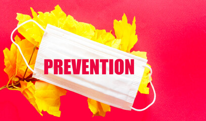PREVENTION, text on a medical mask that lies on a red background next to yellow foliage. Medicine concept