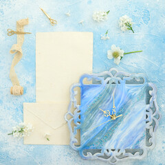 Composition of flowers with paper cards, scissors and resin art wall clock on blue. Flat lay